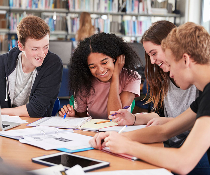 Group of four students studying together at a library table smiling and discussing papers